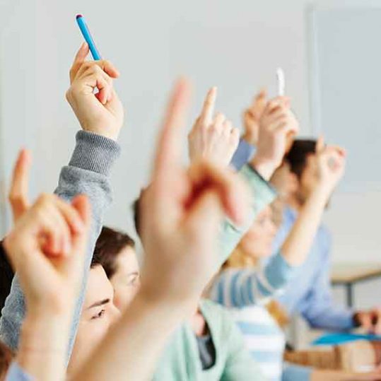 Many students raising their hands in class for an answer